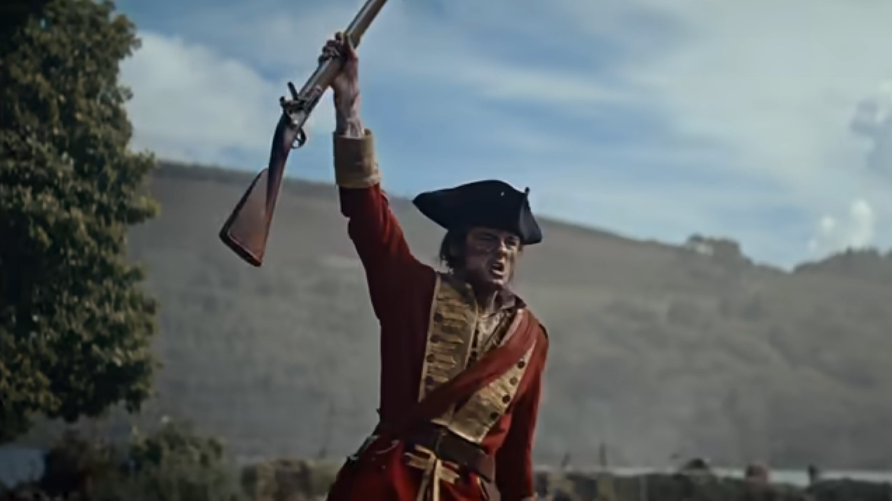 An 18th century soldier lifts his musket in the air in victory