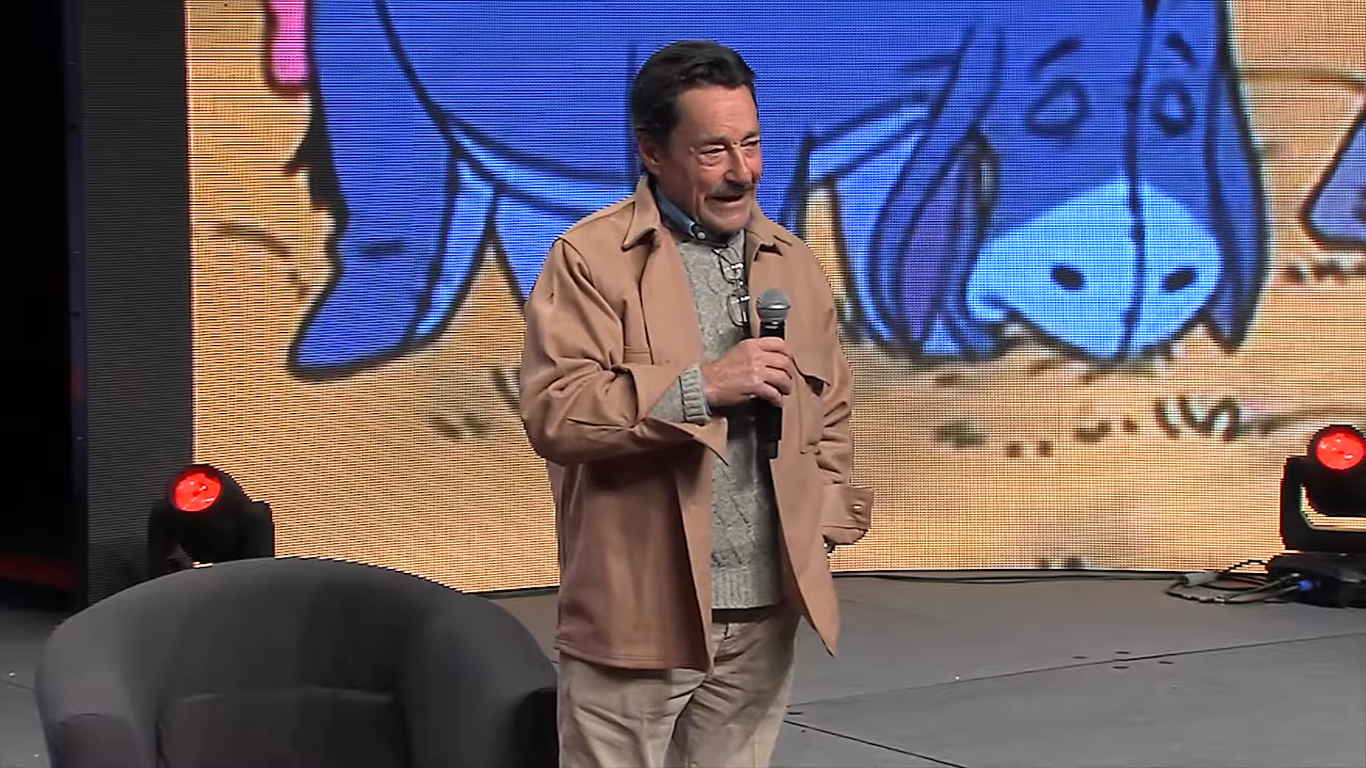 Peter Cullen on a stage, holding a microphone