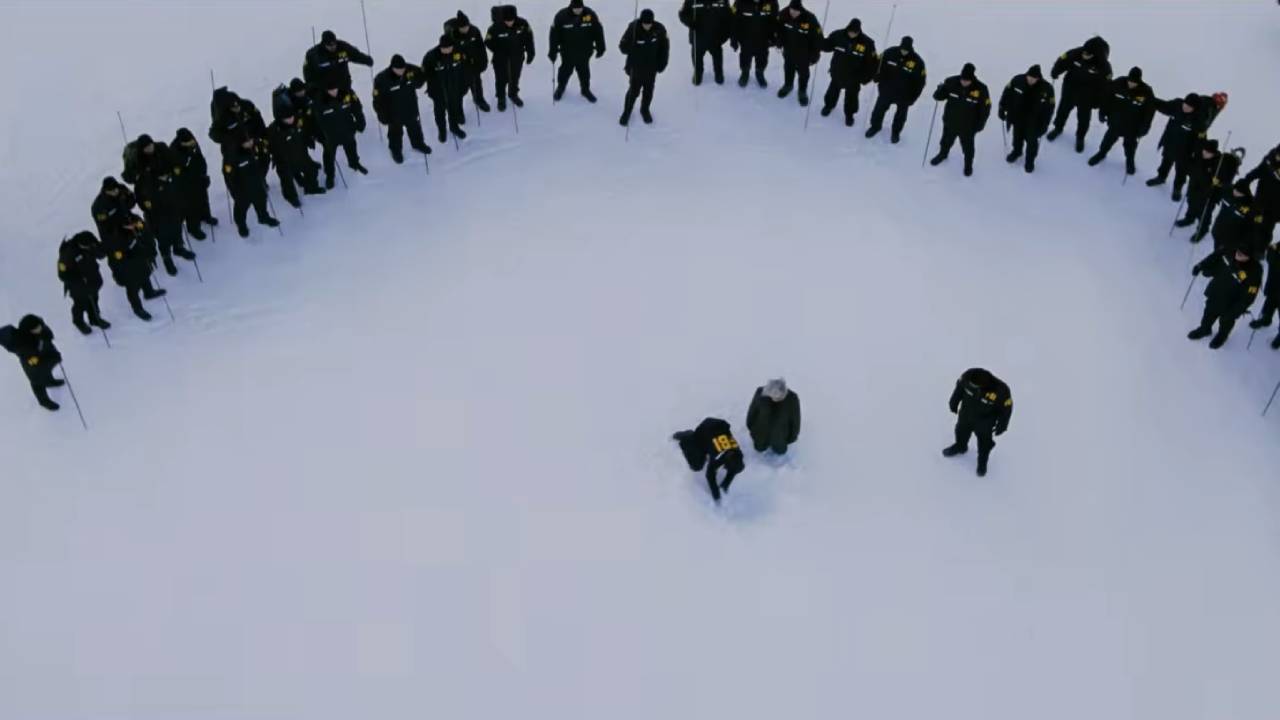 Overhead shot of people dressed in black standing in a half circle on snow