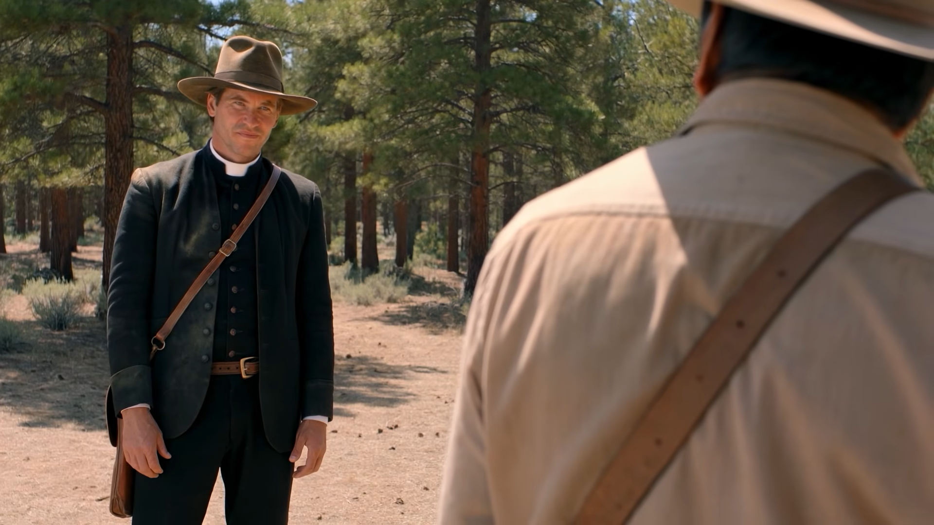 An AI Val Kilmer in a wide-brimmed hat and dressed as a priest, listening to another man