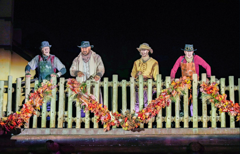 Four men in make-up to look slightly spooky standing behind a fence with fall decor