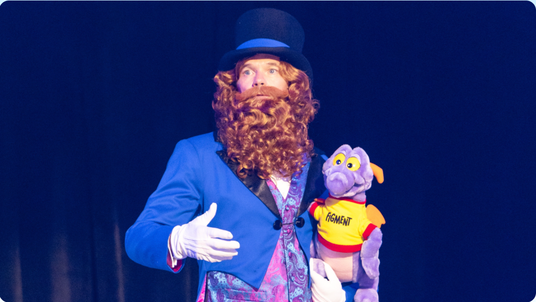 Man in costume beard, top hat, and blue suit holding a purple dragon plush