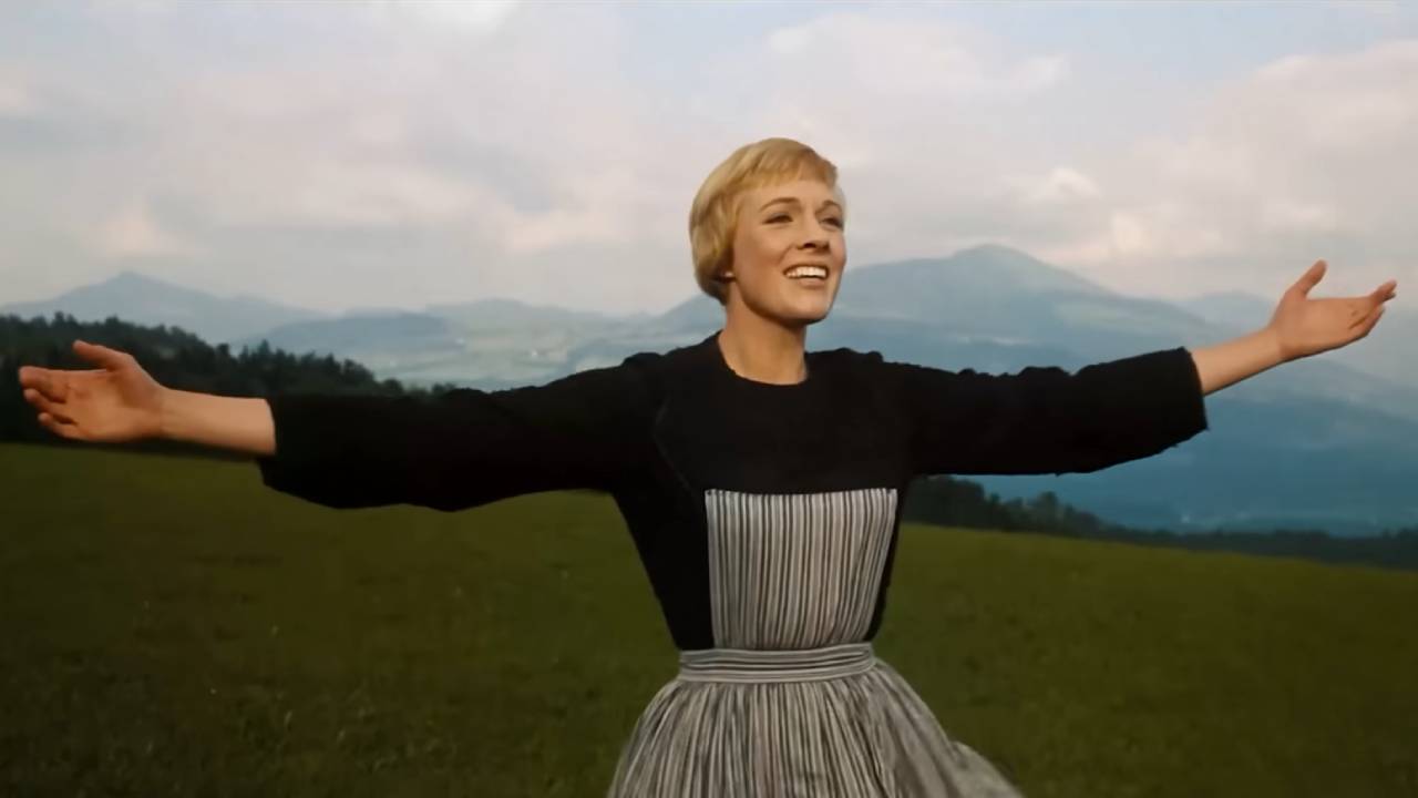 Julie Andrews singing in open field, arms spread wide