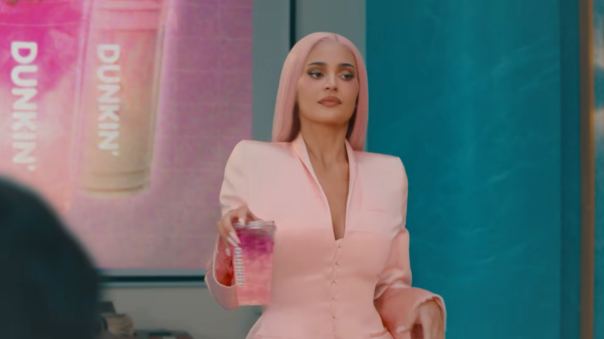 A woman with pink hair and matching blazer holds a drink