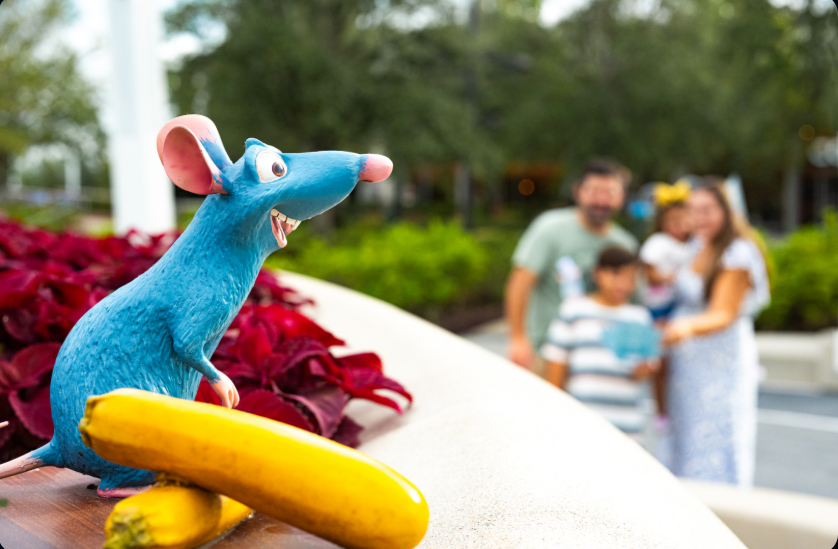 Small gray cartoon mouse statue overlooking family inside theme park