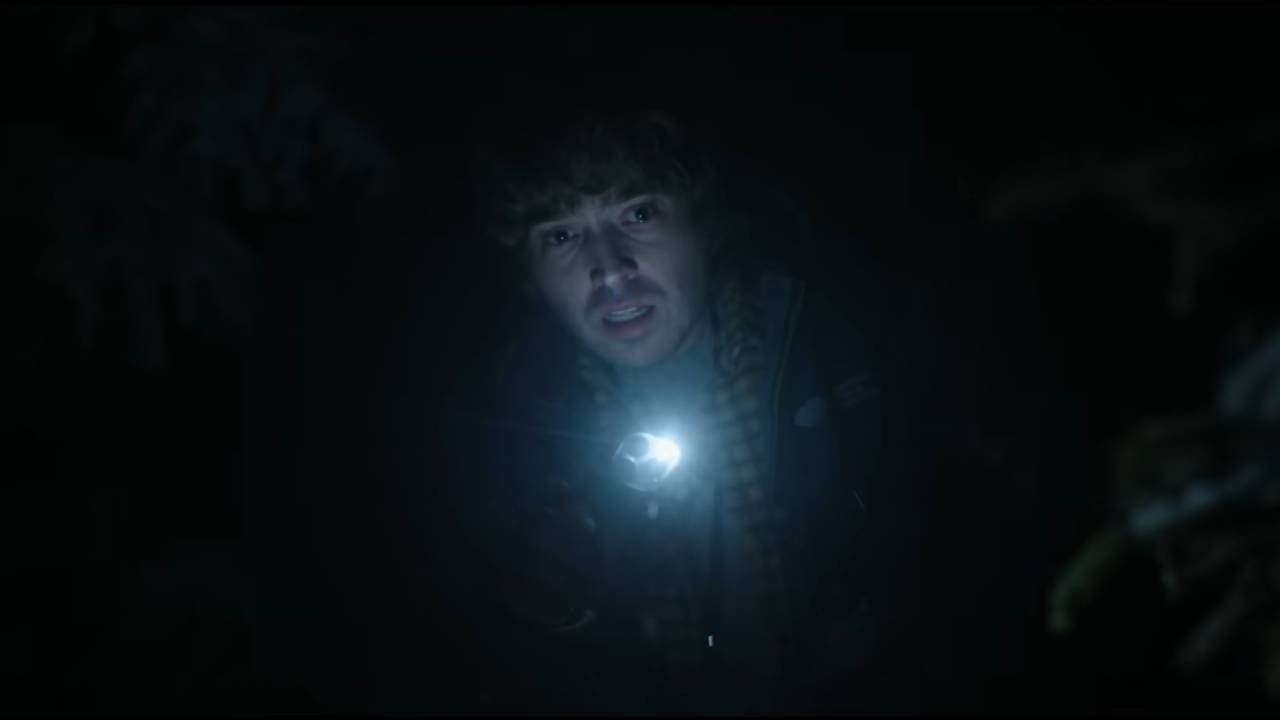 A young man holding a flashlight, surrounded by darkness