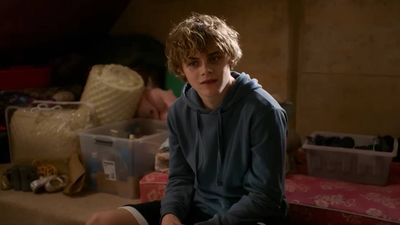 A boy sits on a bed looking confused