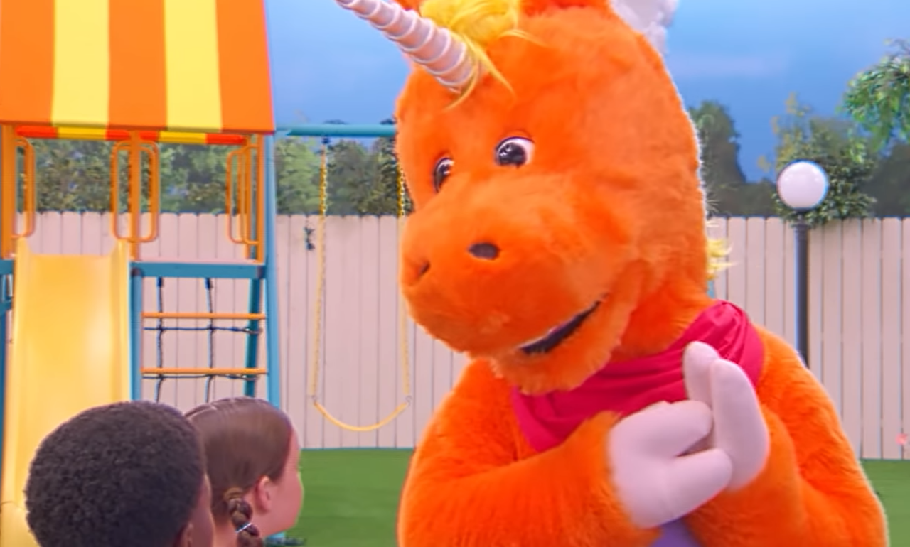 Buddy the Unicorn Large orange unicorn talking to kids on brightly colored TV show set