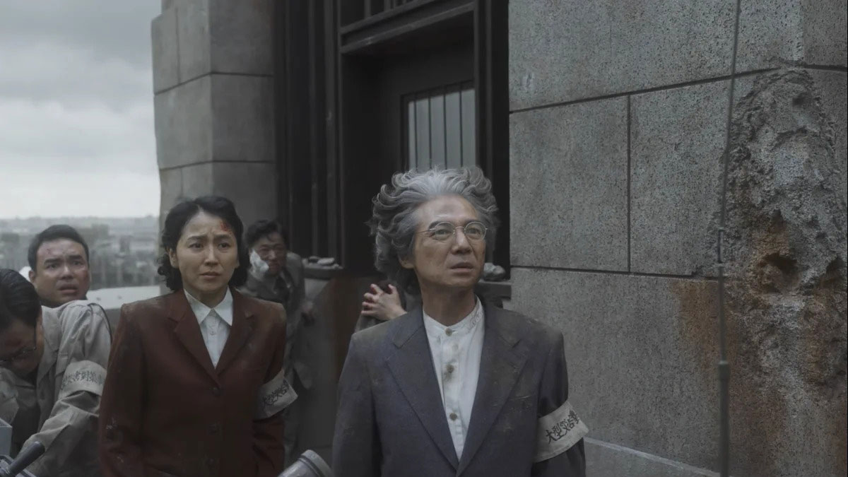 A young woman and an older man stand outside, looking up at something in fear.