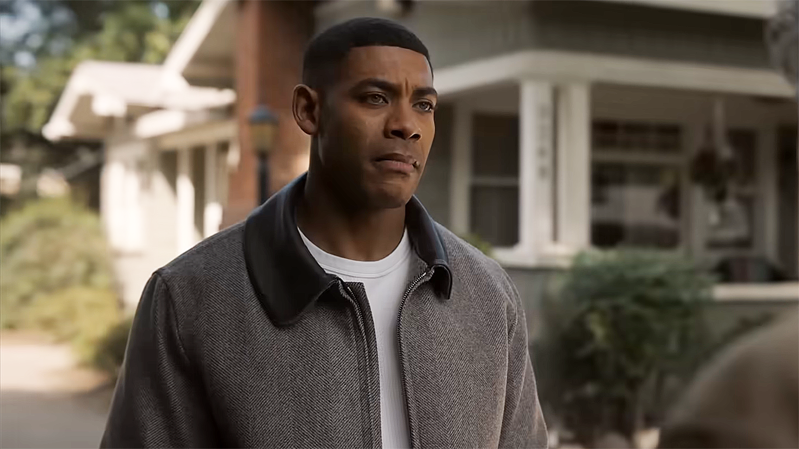 A young man looks somberly into the distance outside a family home