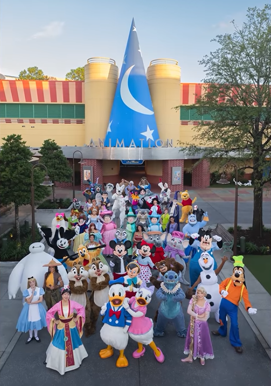 60 Disney characters stand outside the a building with a blue sorcerer's hat