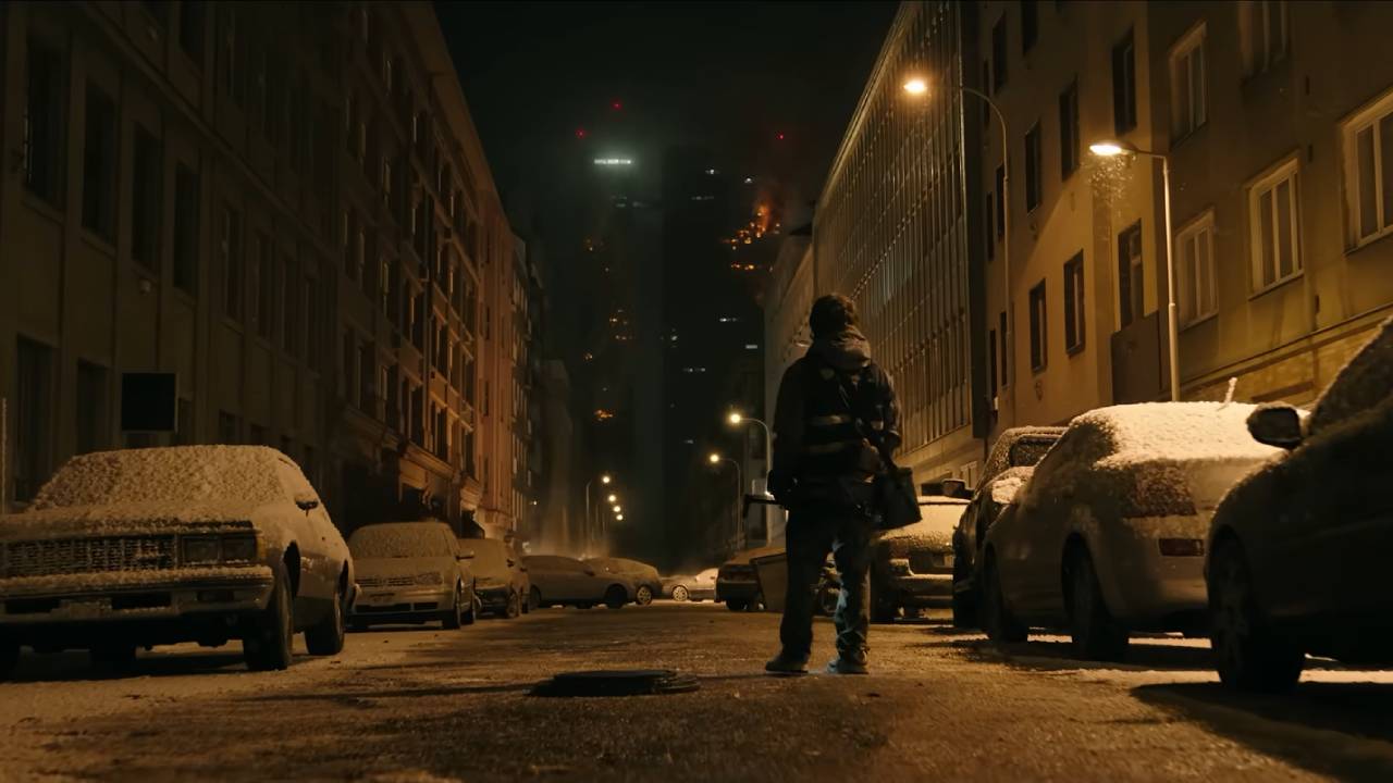 A man walks down a city street at night, the cars covered in snow.