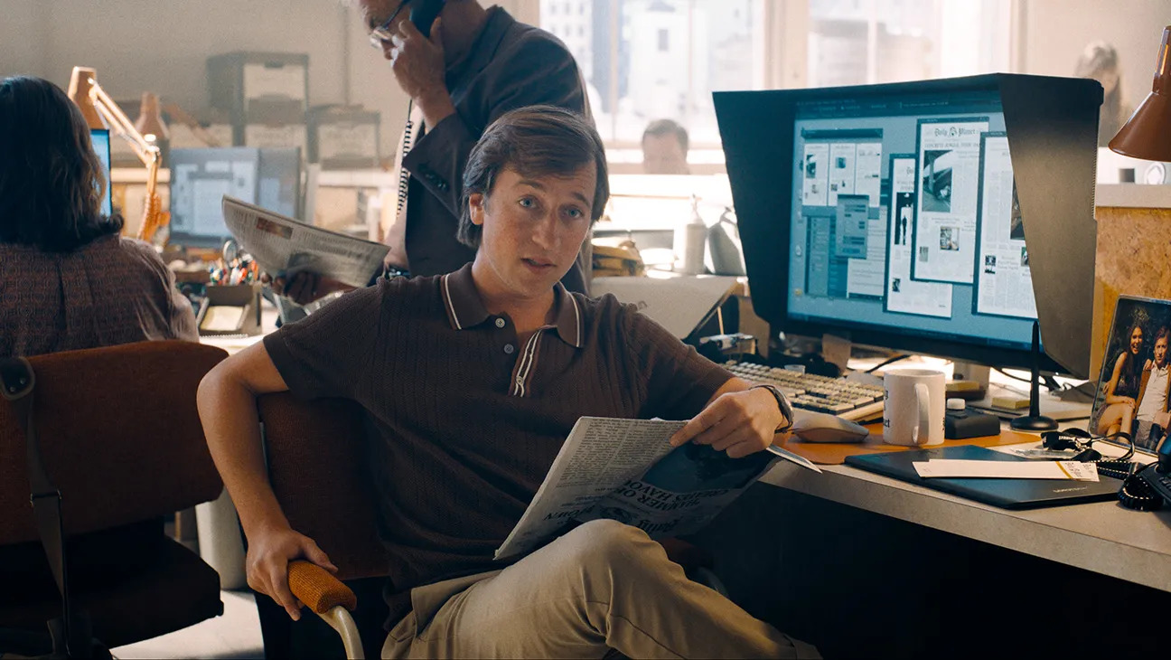 Jimmy Olson sits at a desk in a newsroom, asking a question