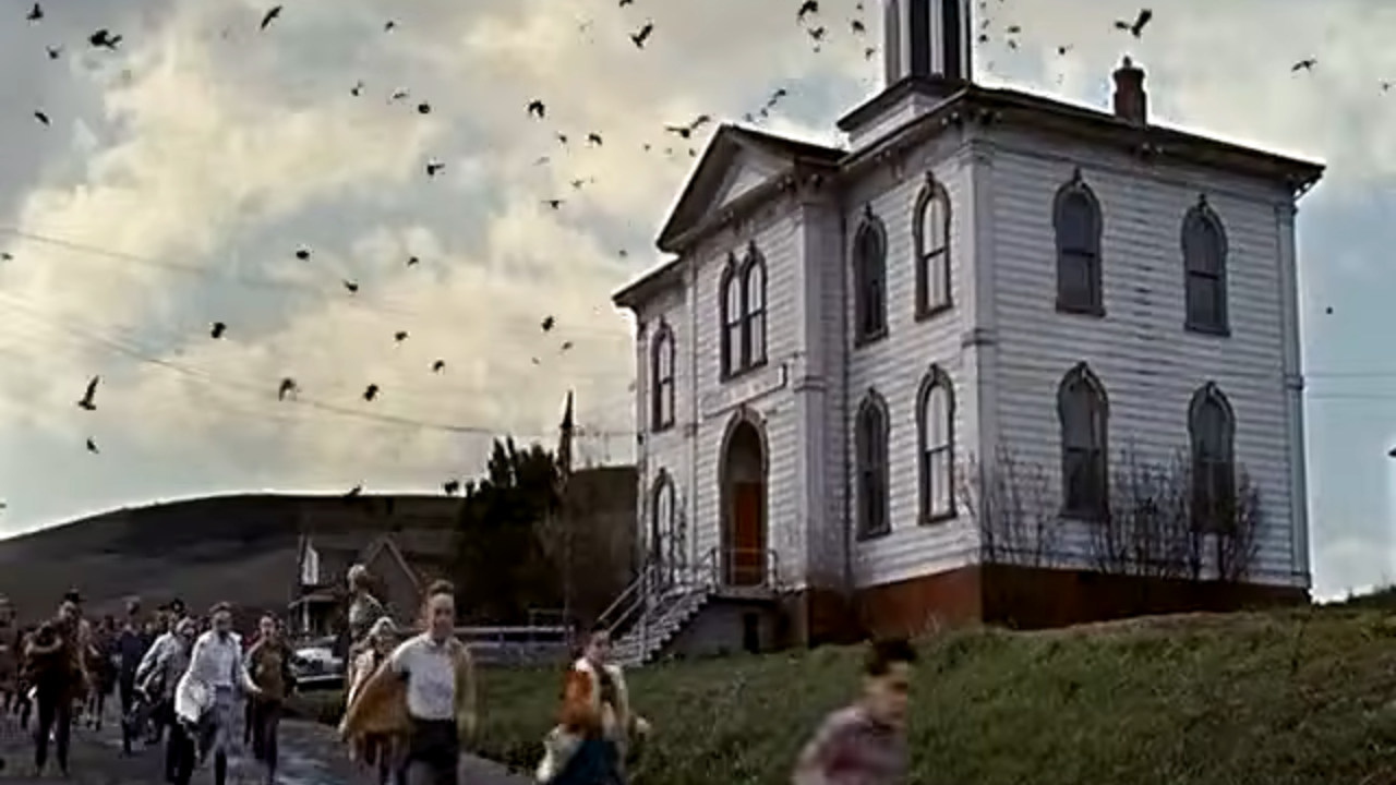Children run down a street past a large schoolhouse, screaming as they are attacked by birds