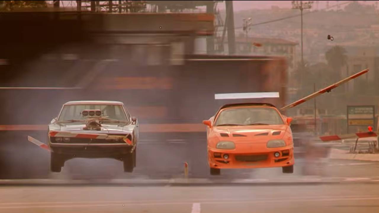Two sports cars fly through the air after narrowly missing a speeding train
