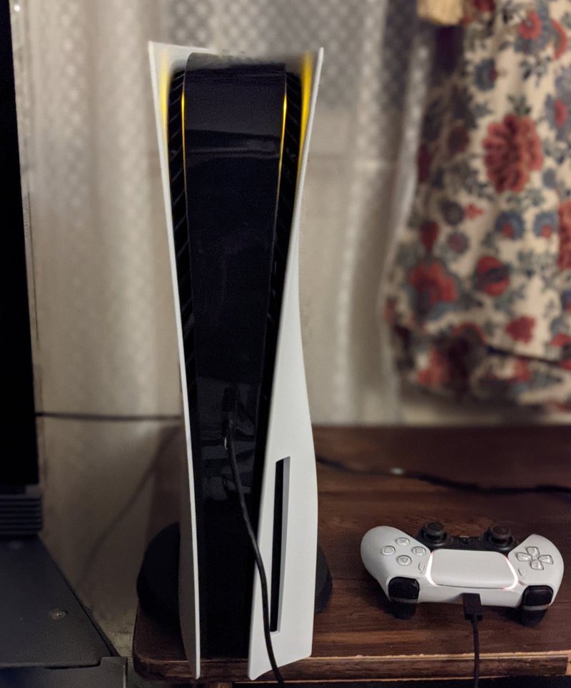 A white PlayStation 5 console standing upright next to a DualSense controller