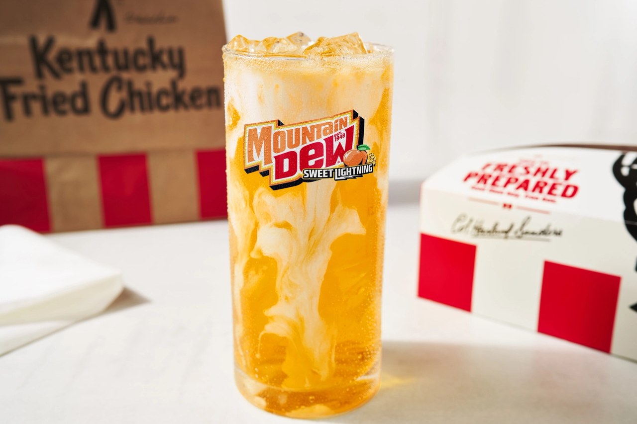 A tall glass of peach soda swirled with vanilla cream beside a KFC bag and box