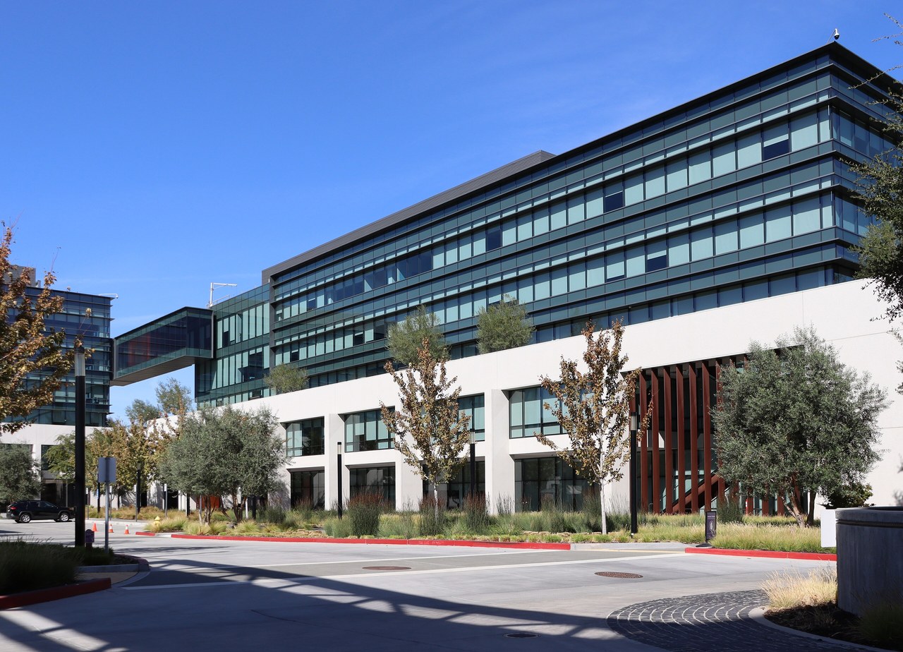 A modern multistory office building with glass windows behind trees on Coleman Avenue in San Jose