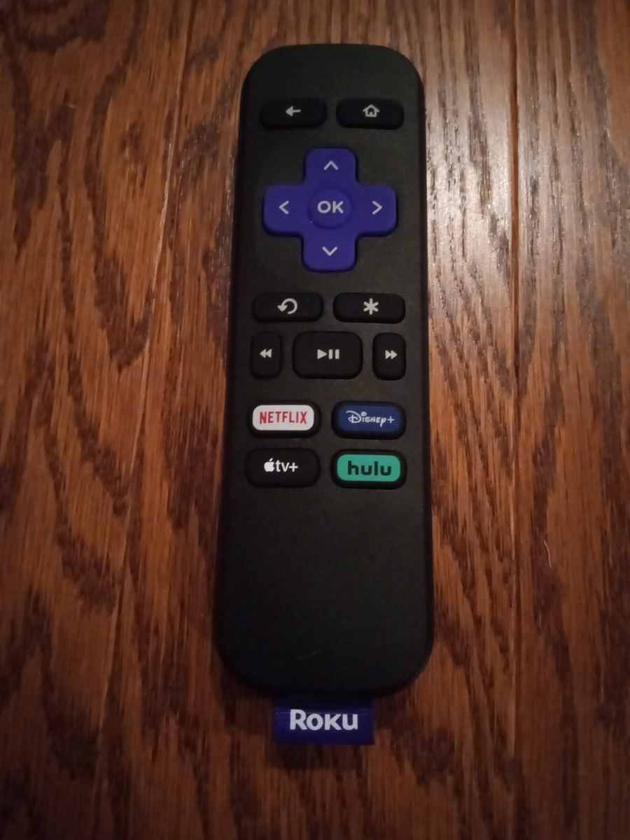 A black Roku TV remote with a purple directional pad lying on a wooden surface