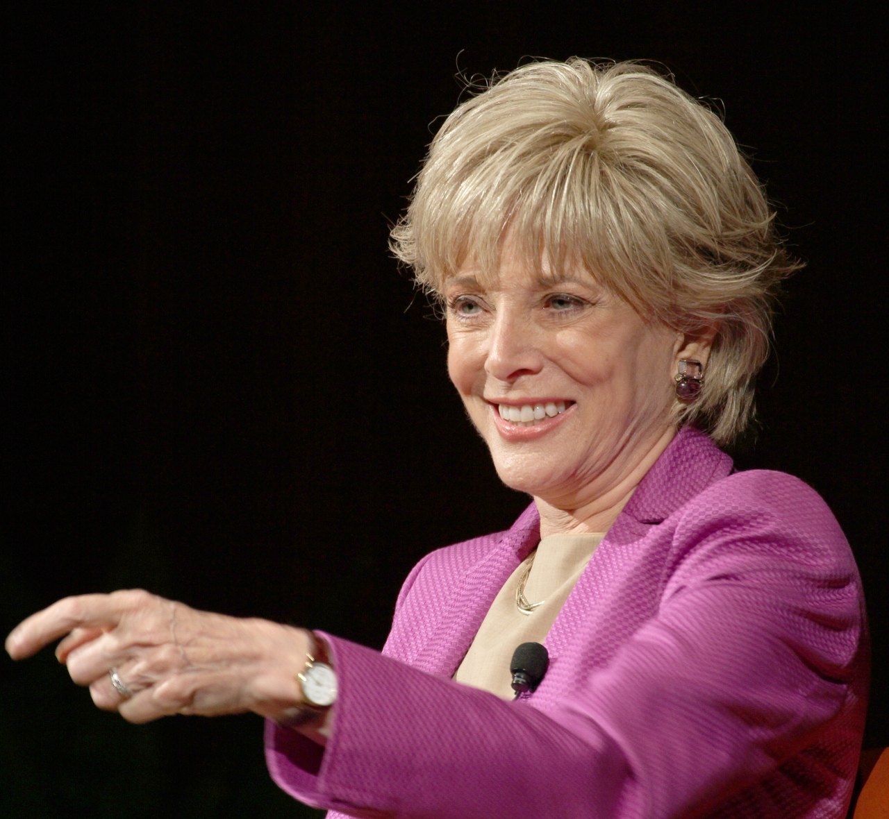Lesley Stahl in a pink jacket smiling and gesturing while speaking on stage