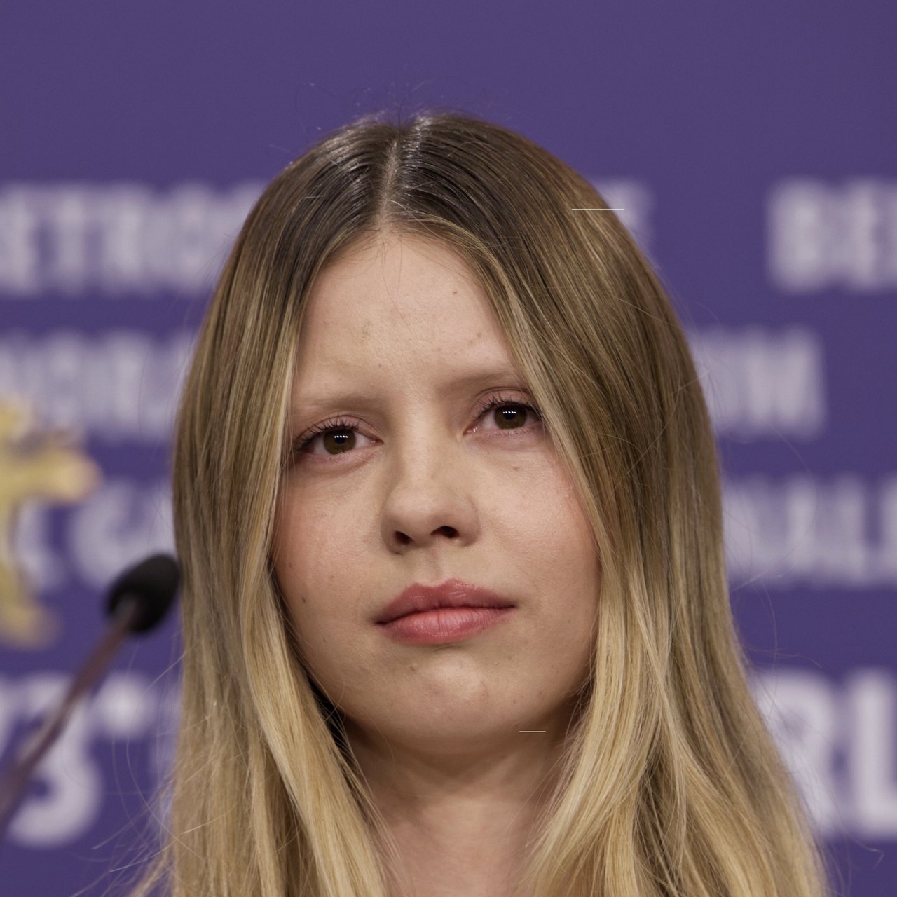 Mia Goth with long blonde hair seated in front of a purple Berlinale backdrop