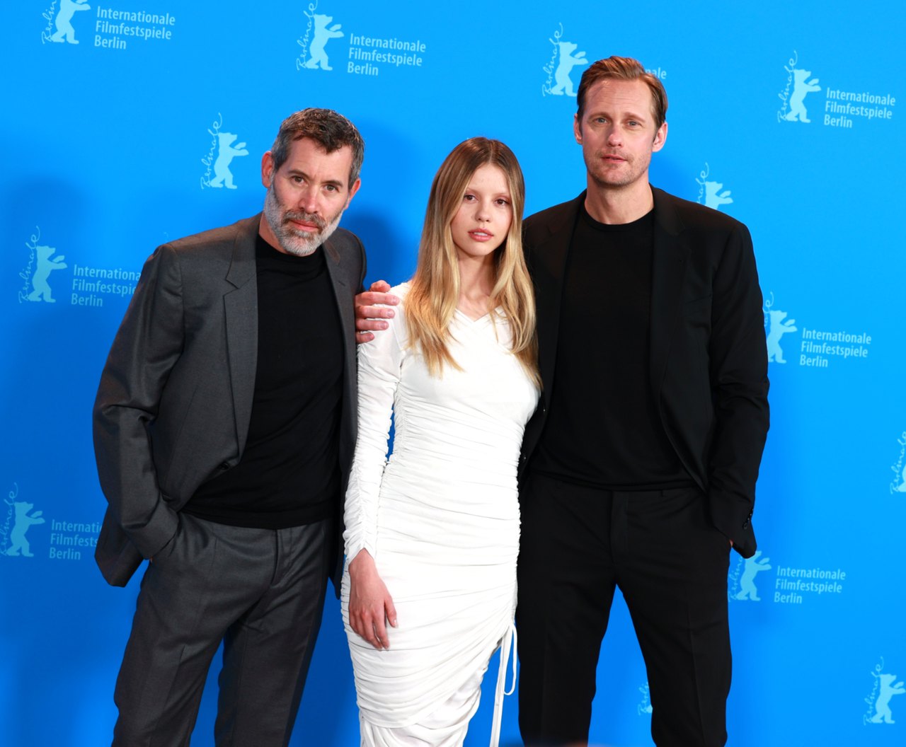 Jalil Lespert, Mia Goth, and Alexander Skarsgård posing together in front of a blue Berlinale backdrop