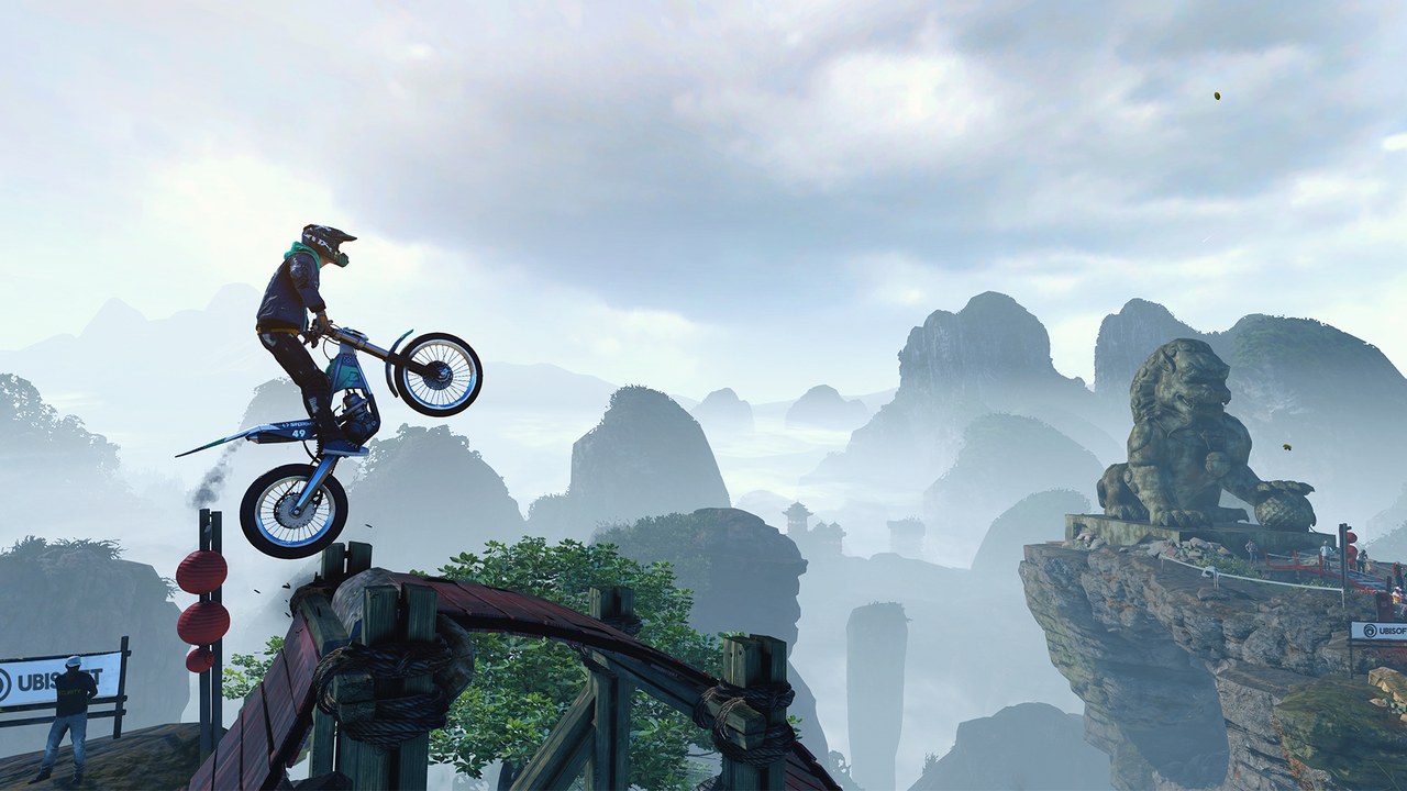 A motorbike rider balances on a narrow ledge above misty mountains
