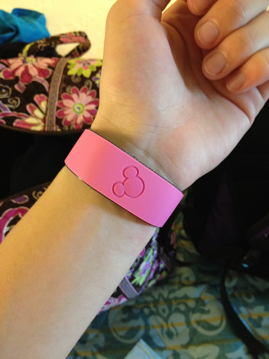 A pink MagicBand with a Mickey Mouse icon worn on a guest's wrist