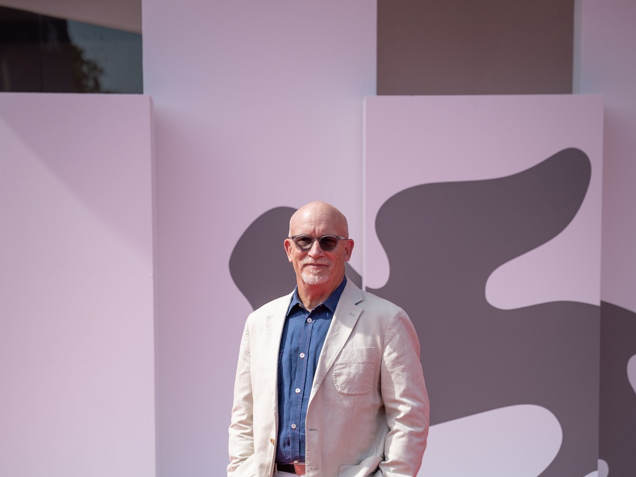 Alex Gibney in a light suit jacket standing in front of a pink festival backdrop