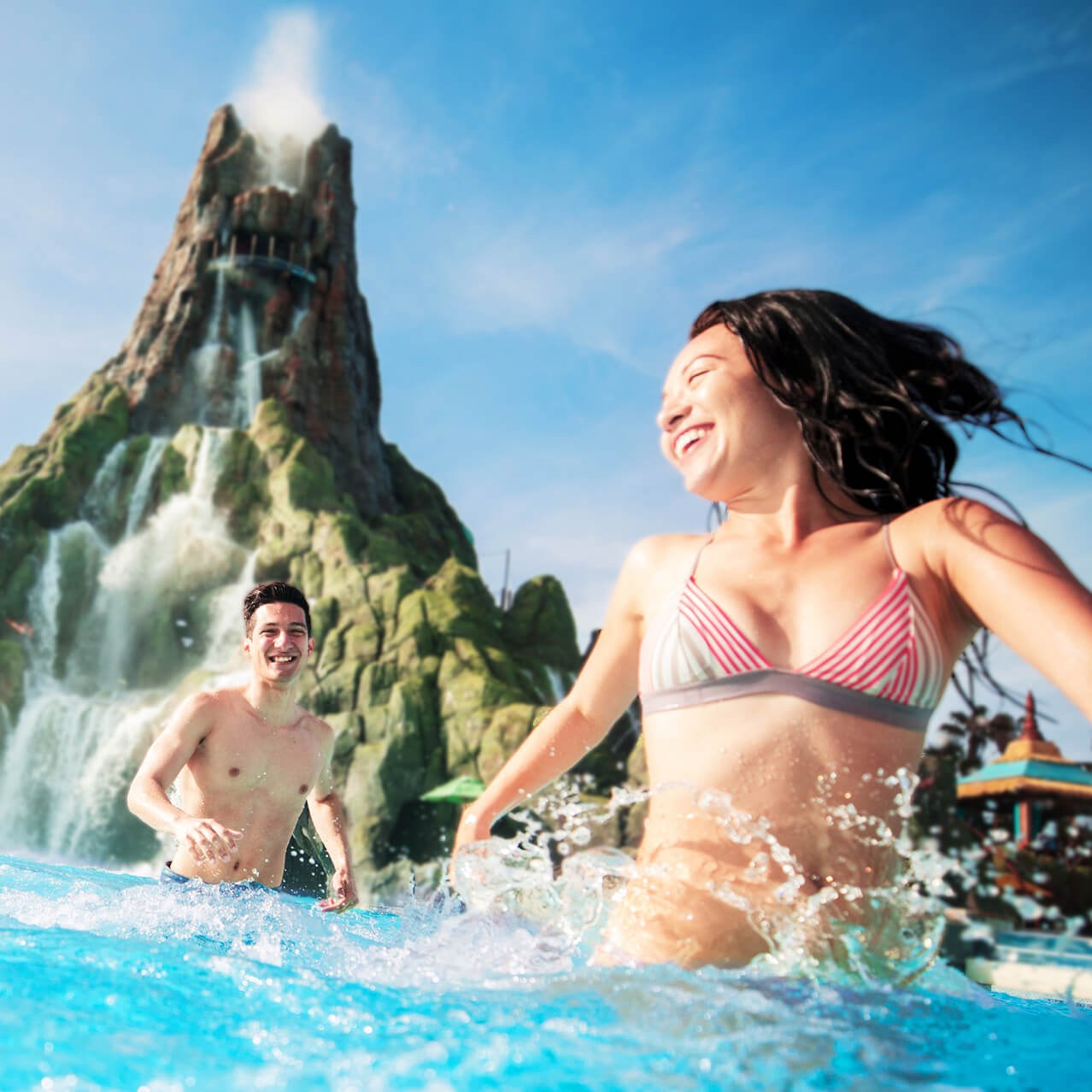 Two guests splashing in the wave pool at Waturi Beach with the Krakatau volcano behind them